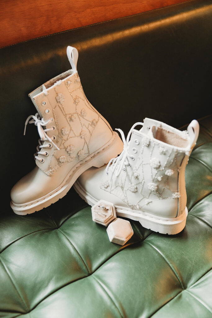 Close up detail shot of white combat boots with lace and a pink velvet ring holder on a green leather couch.