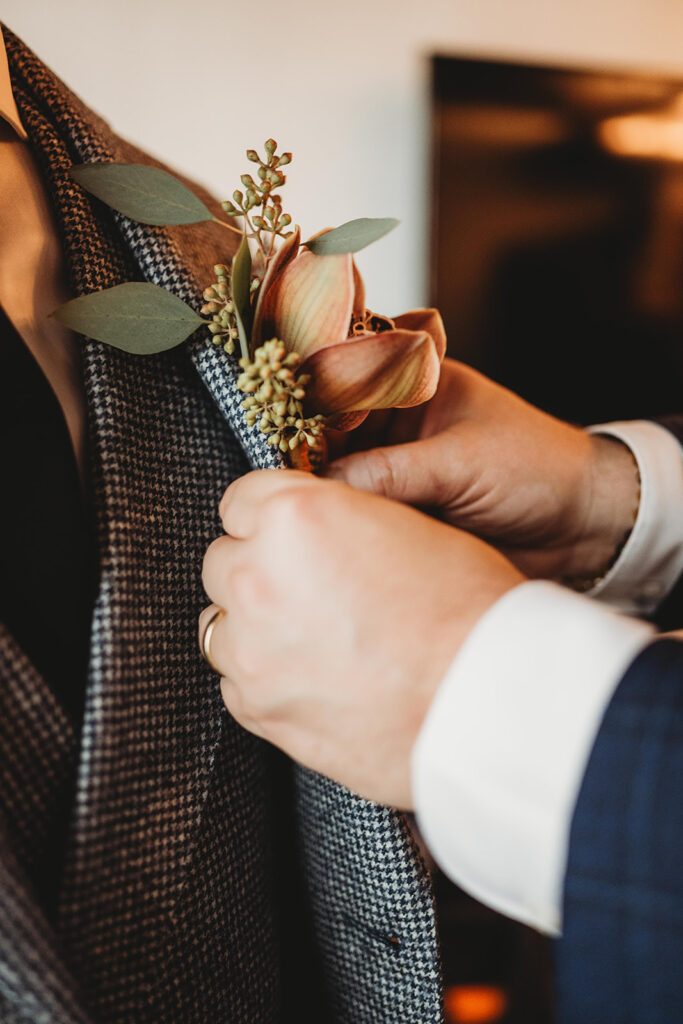 Close up photo of best man adjusting groom's boutonnière on his suit jacket