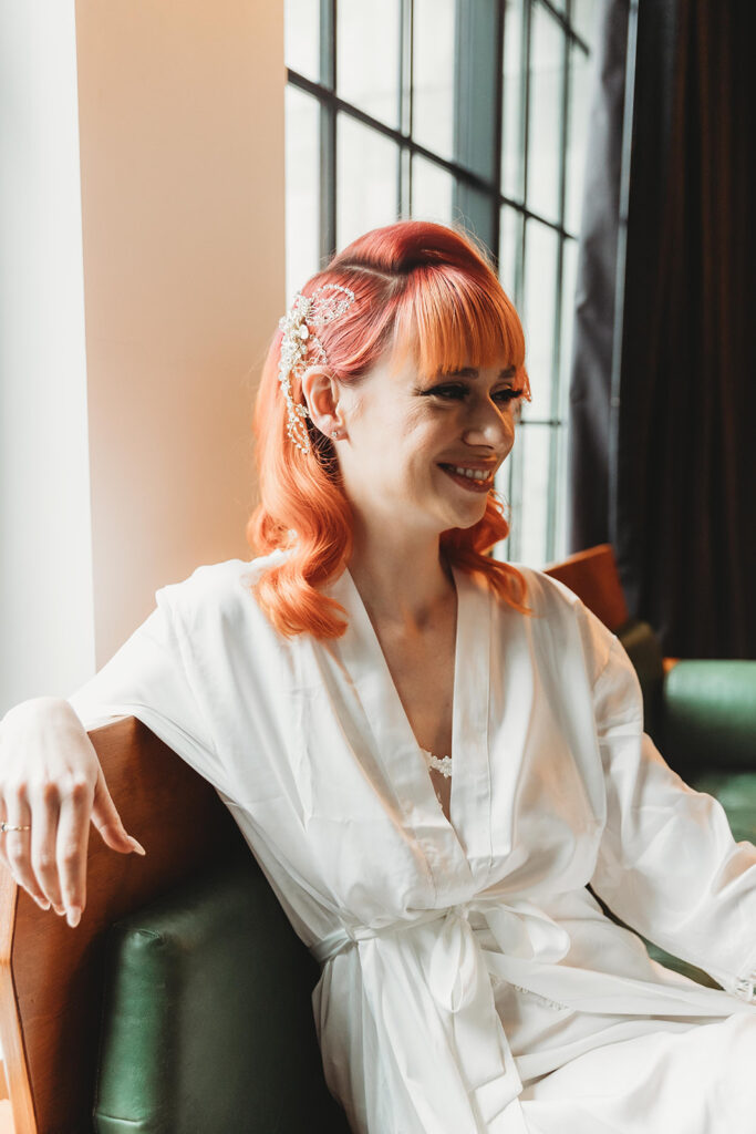 Close up photo of the bride sitting on the green leather couch with hair and makeup complete in a white silky robe.