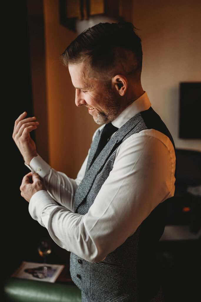 Photo of groom turned to the side adjusting his cuff links