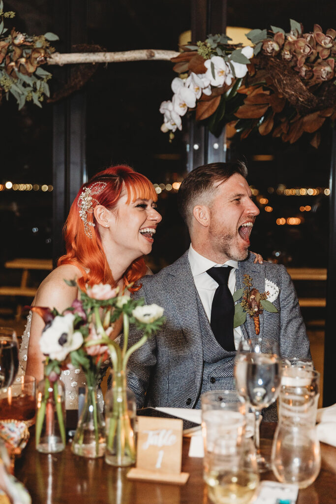 Bride and groom listening to speeches and laughing big